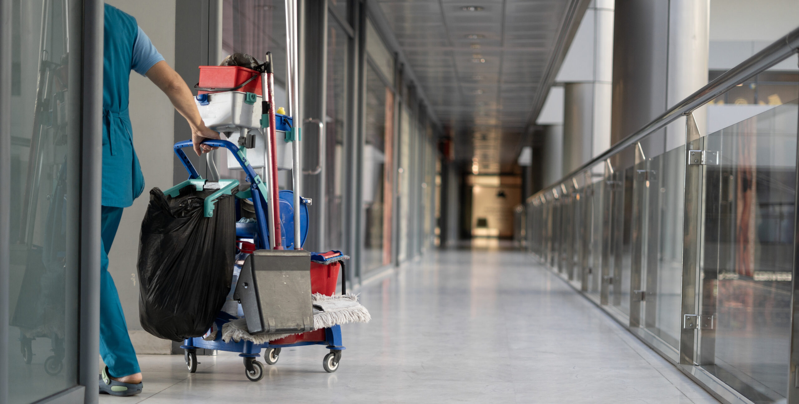 Cleaner moving a janitorial trolley through a retail arcade during after-hours cleaning