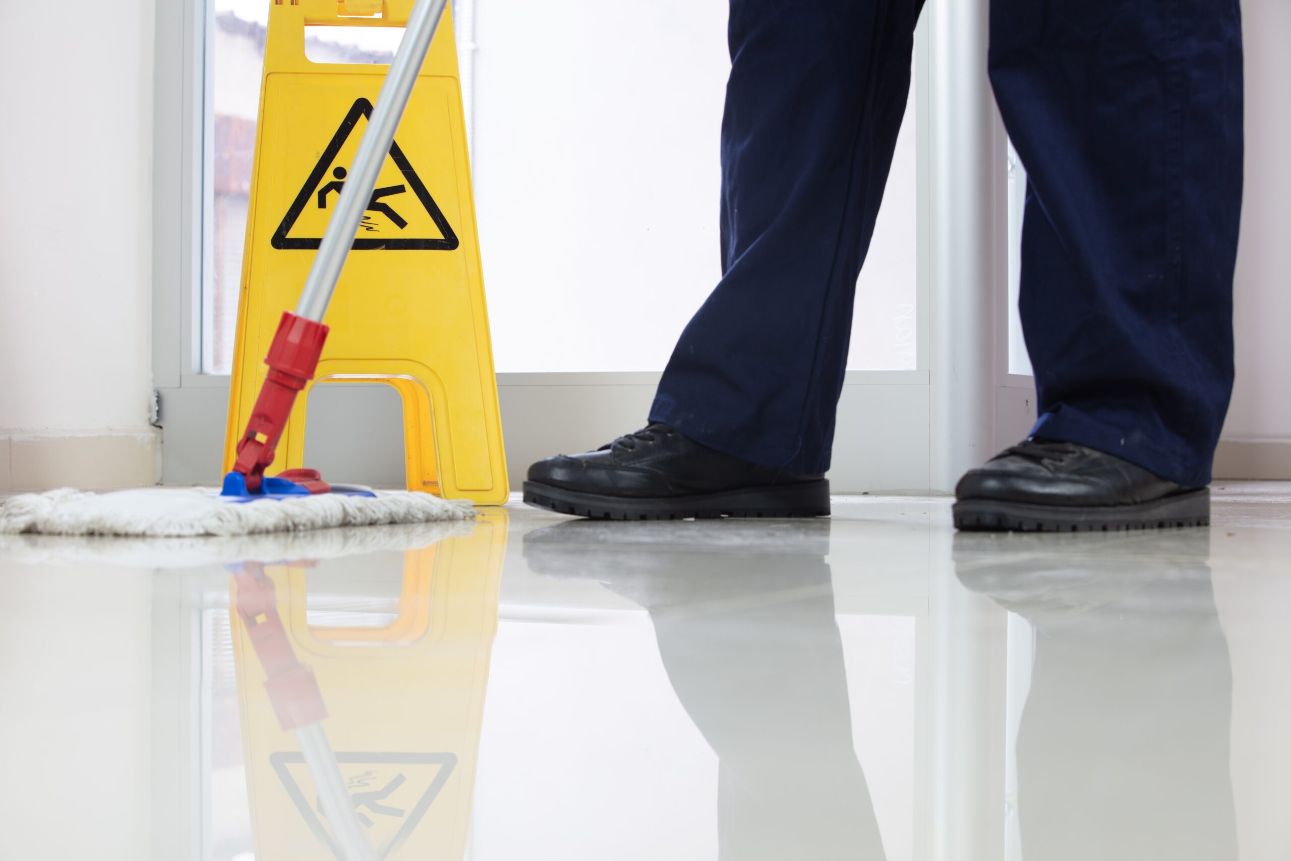 Cleaner mopping a polished retail floor beside a yellow caution wet floor sign to prevent slip hazards