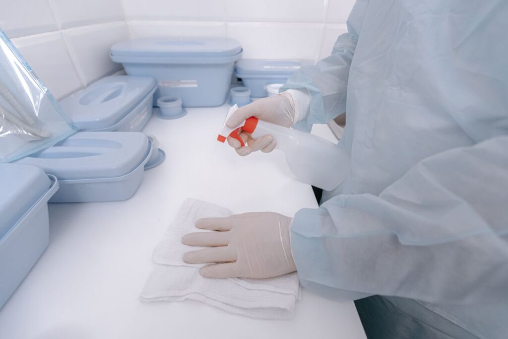 Healthcare worker in protective gown and gloves performing clinical surface sanitisation in a medical facility